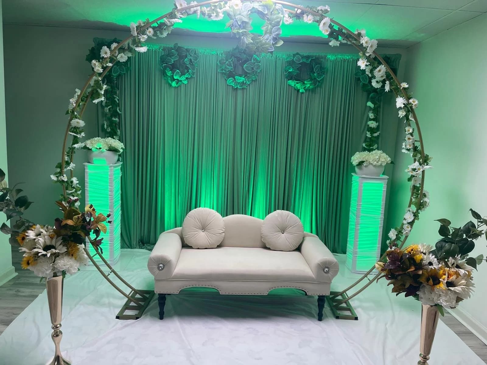 Elegant wedding stage with circular floral arch, loveseat, and green uplighting